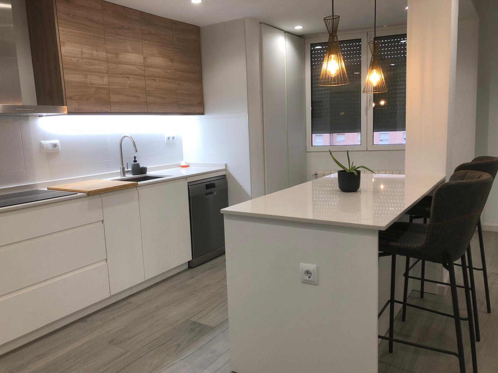 Cocina blanca con península, taburetes y módulos altos en madera